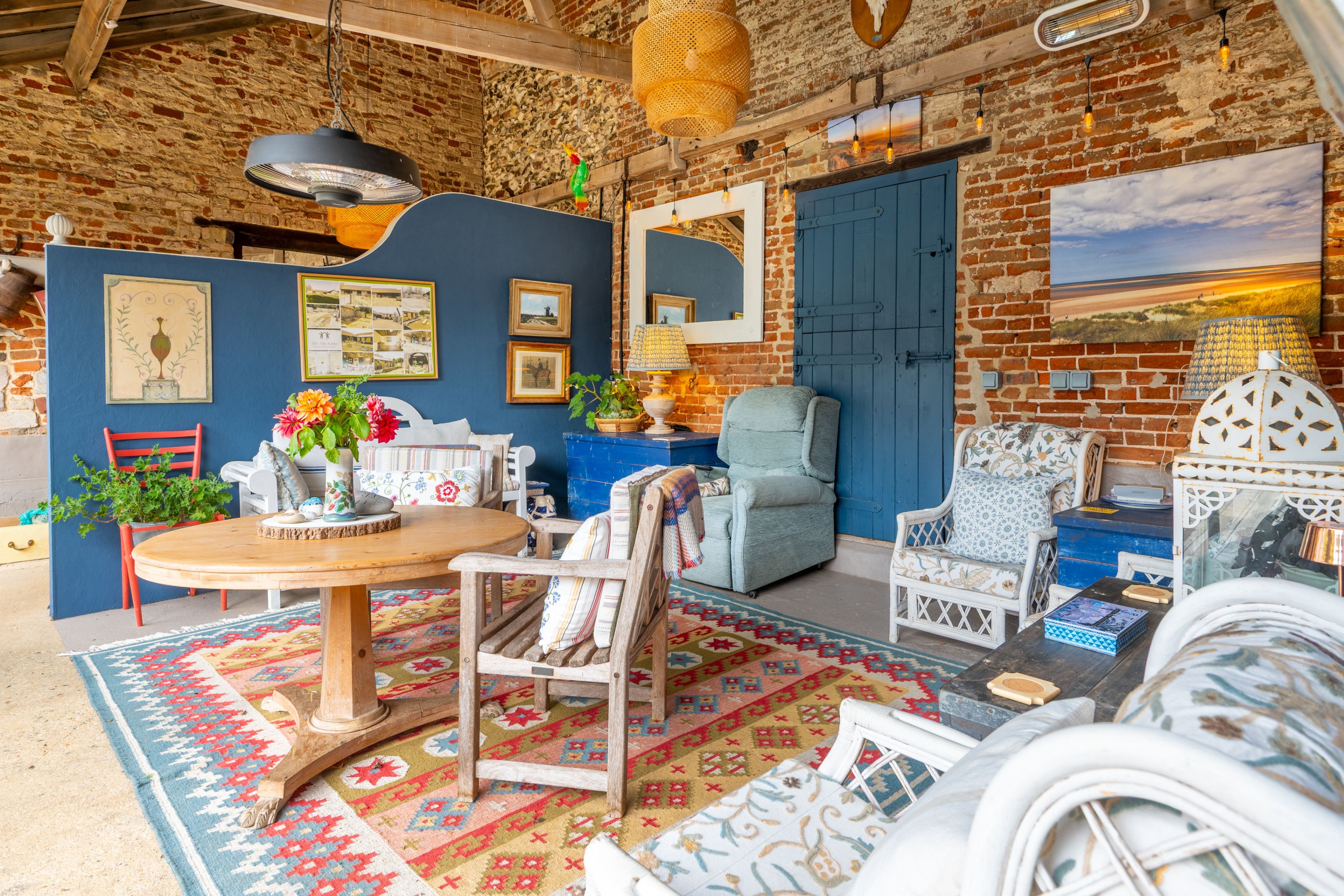 A rustic interior with exposed brick walls, a round wooden table, and a variety of seating options including a blue armchair and a white patterned chair.