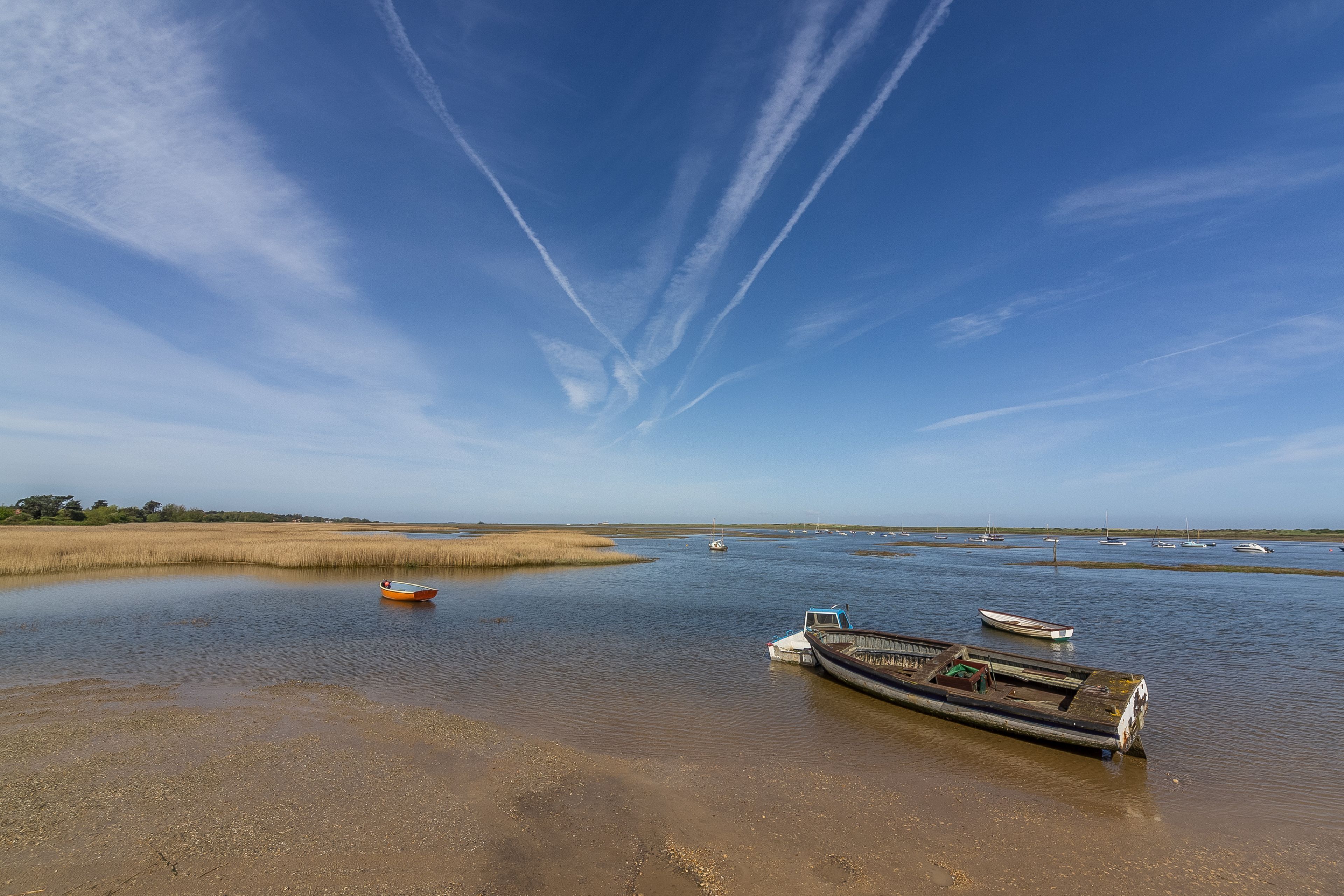 A calm water body with boats, a clear sky, and distant trees.