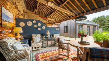 A covered outdoor seating area with wicker furniture, a patterned rug, and a view of a wooden building.