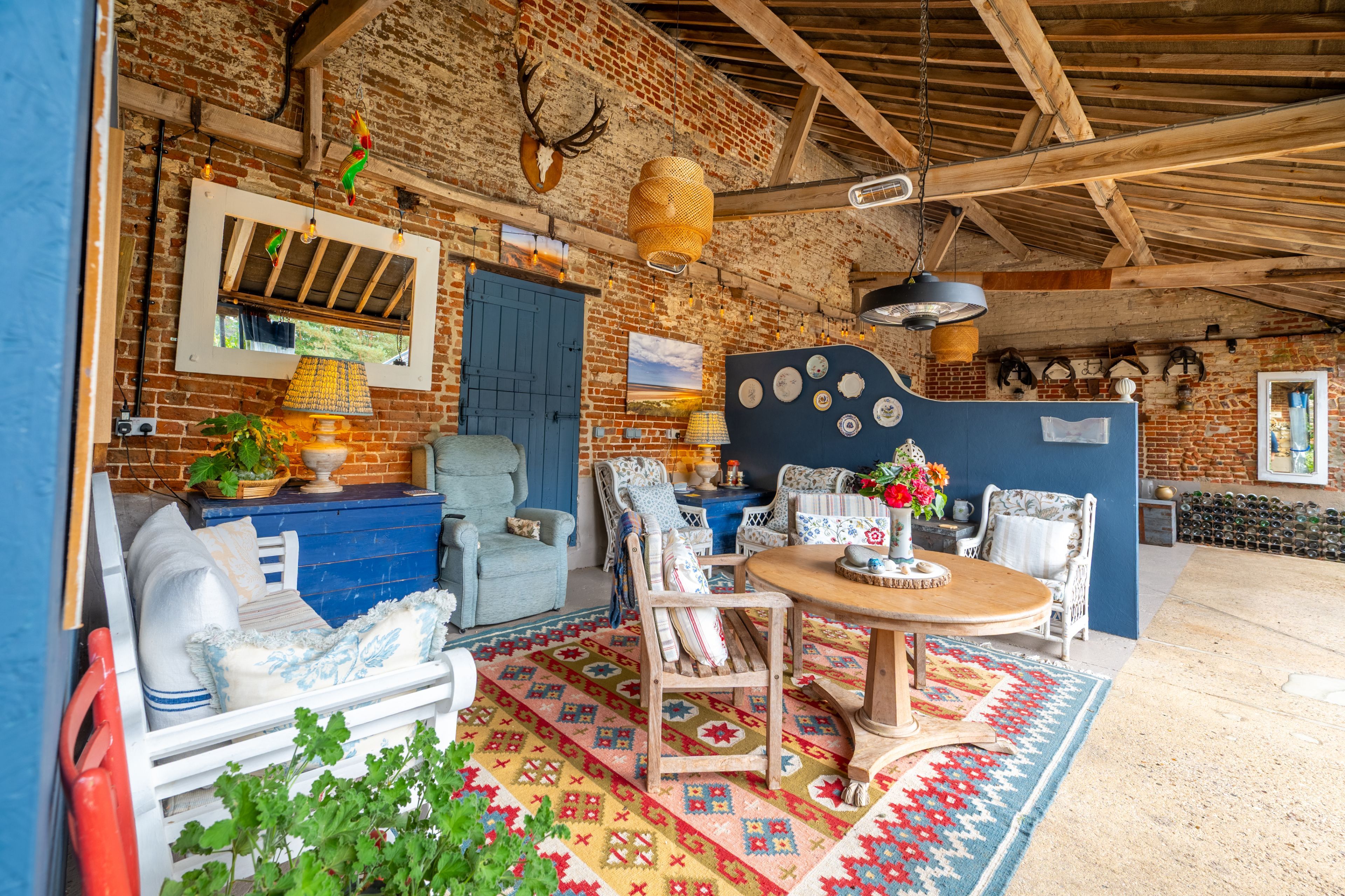 A rustic interior with exposed brick walls, wooden beams, a blue door, and a dining area with a patterned rug.