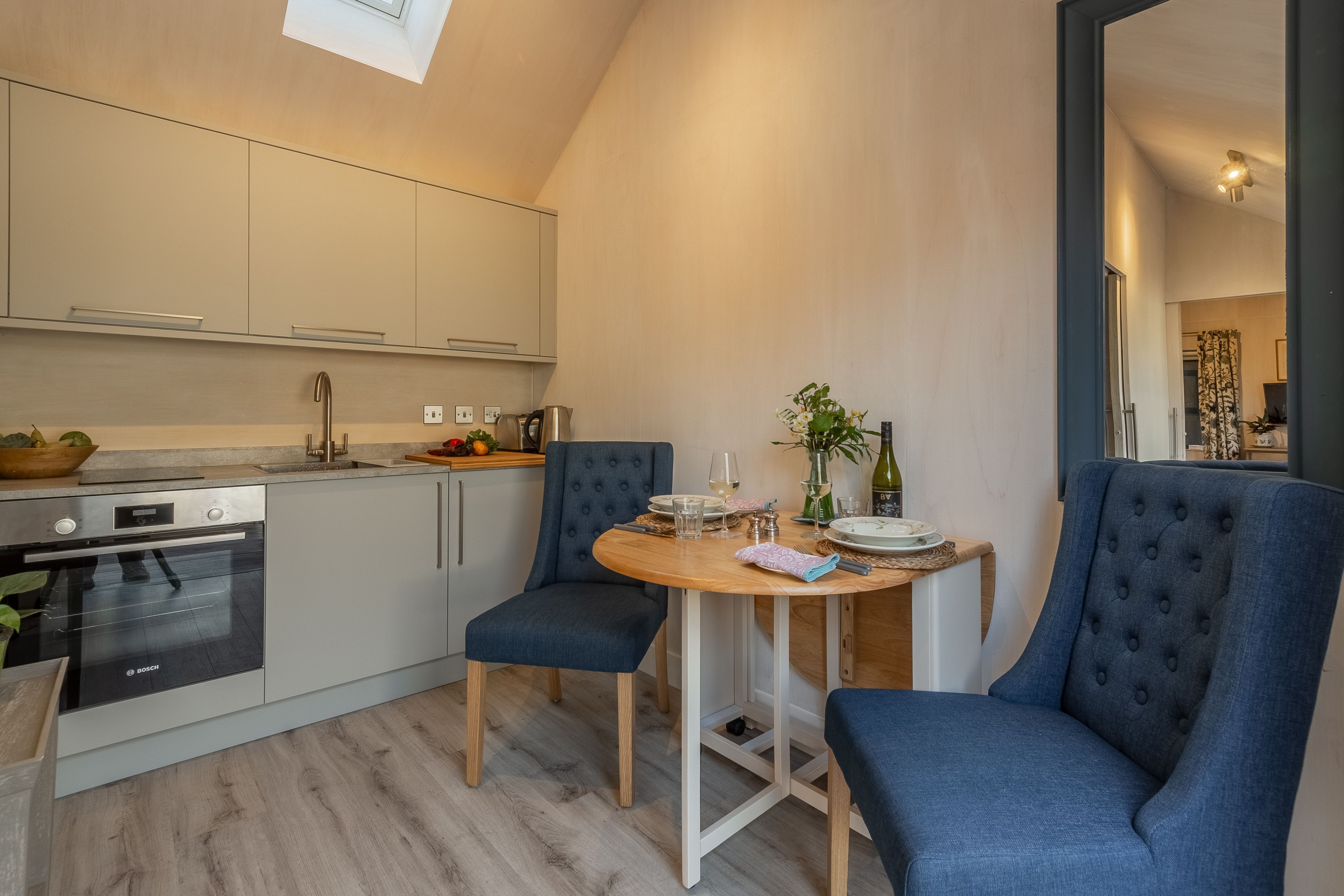 A compact kitchen with modern appliances, a dining area with two chairs, and a small table set for two.
