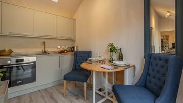 A compact kitchen with modern appliances, a dining area with two chairs, and a small table set for two.