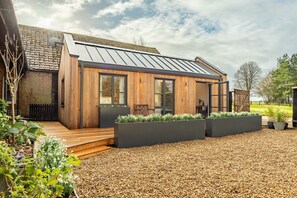 Een modern huis met een schuin metalen dak, houten gevel en grote ramen.