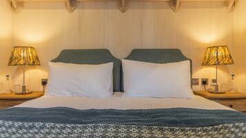 A double bed with a patterned bedspread, two bedside lamps, and a wooden shelf above the bed.