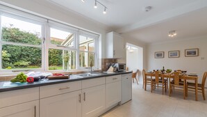 Une cuisine moderne avec des meubles blancs, une grande fenêtre et un coin repas doté de chaises en bois.