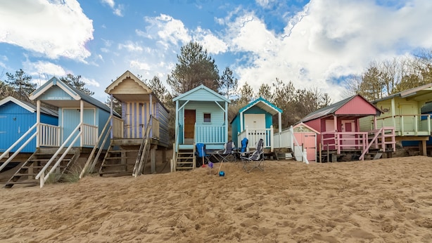 Une rangée de cabanes de plage, avec des escaliers en bois menant à chacune d’elles, est située sur une plage de sable.