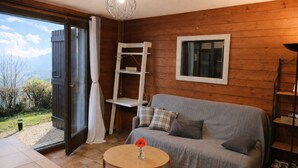 Ein Zimmer mit Holzvertäfelung, einer Couch, einem kleinen Tisch mit Blumenvase, einer Leiter und einem Fenster mit Blick ins Freie.