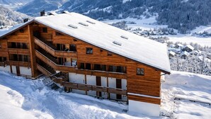 Eine Holzhütte mit Balkon, vor einer verschneiten Berglandschaft.