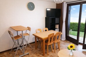 Une pièce comprenant une table à manger, des chaises, un téléviseur et une porte-fenêtre coulissante donnant sur un jardin.