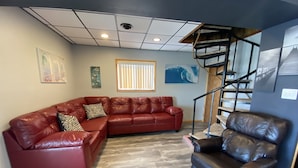 A living room with a red leather sectional sofa, a brown leather armchair, a wooden staircase, and a large window with blinds. - Water Front Vacation Home (Clay Township)