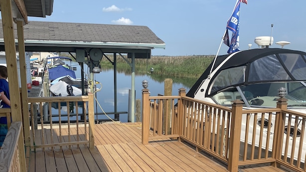 A wooden deck with a covered area and a boat docked nearby. - Water Front Vacation Home (Clay Township)