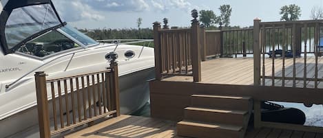 Una terraza de madera con un barco amarrado a la izquierda, barandilla de madera y cielo despejado.