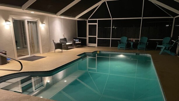 Una piscina con una veranda coperta, sedie e una porta che dà su un ambiente interno.