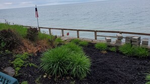 A waterfront view with a wooden deck, a flag, and lush greenery. - Cottage on Lake Erie with beach access .Local wineries (North East)