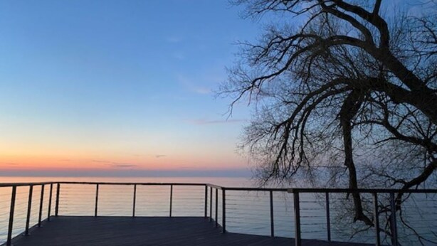 A wooden deck with a metal railing overlooking a body of water during sunset. - Cottage on Lake Erie with beach access .Local wineries (North East)