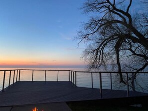 A wooden deck with a metal railing overlooking a body of water during sunset.