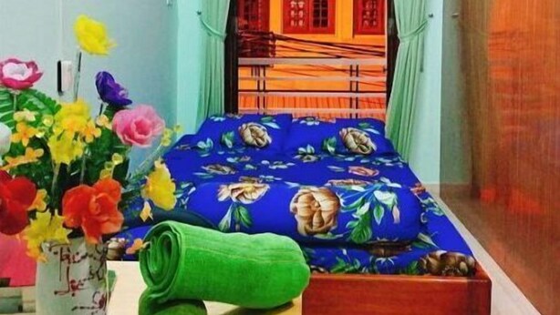 Une chambre à coucher avec un lit, un climatiseur fixé au mur, une fenêtre avec des rideaux et un vase rempli de fleurs.