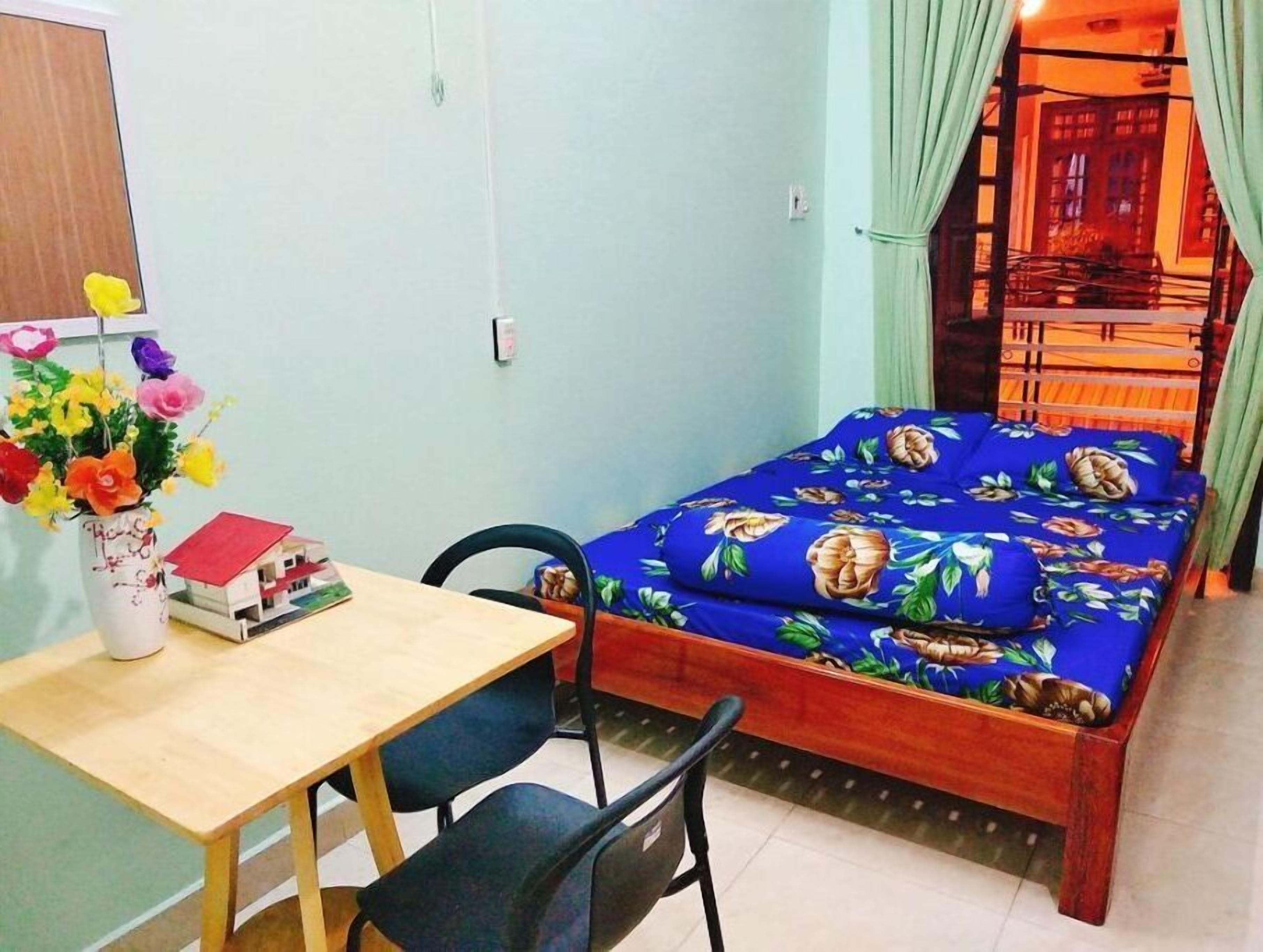 Une petite pièce comprenant un lit, un bureau et une chaise. Un vase rempli de fleurs est posé sur le bureau.
