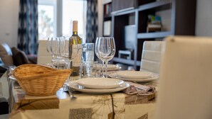 A dining table set with plates, glasses, and a bottle, with a basket and a chair visible. - The Cove of Mogro (Mogro)