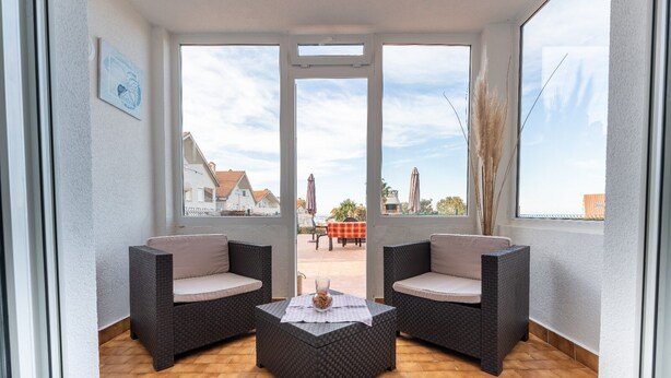 A balcony with wicker furniture, a table, and a view of buildings and a beach. - The Cove of Mogro (Mogro)