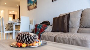 A living room with a sofa, a coffee table with a pine cone and snacks, and a plaid blanket. - The Cove of Mogro (Mogro)