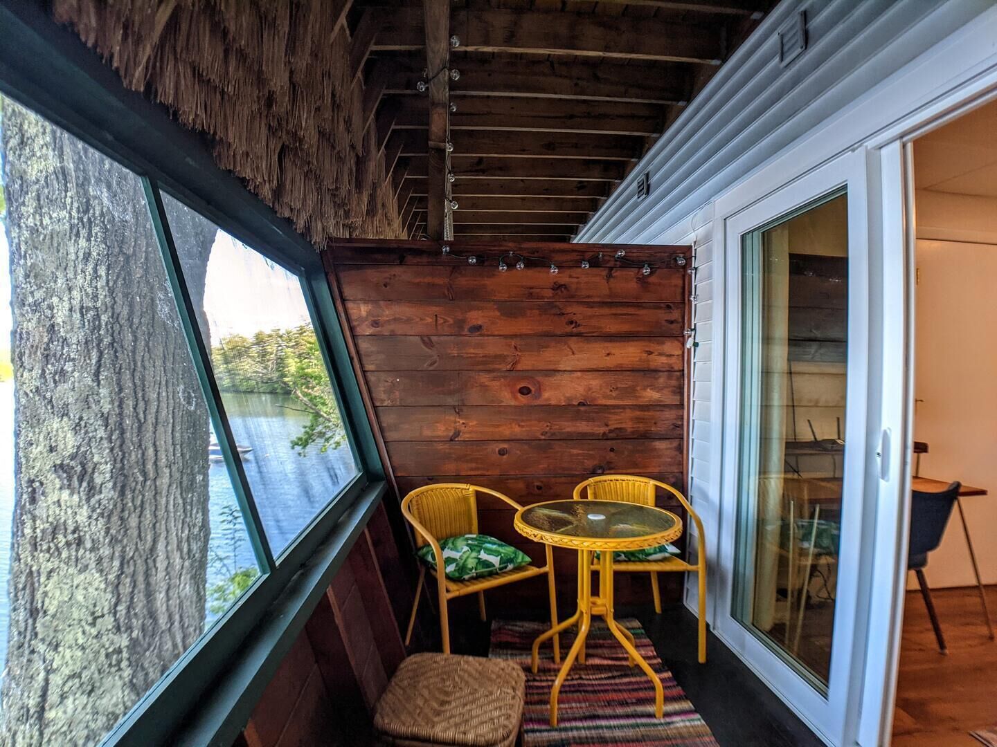 A wooden deck with a glass door leading to a room, two wicker chairs, and a small table.