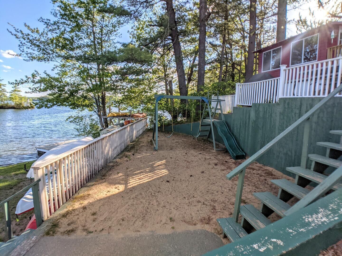 Une zone de plage sablonneuse avec une balançoire, un petit toboggan et une terrasse en bois dotée de rampes.