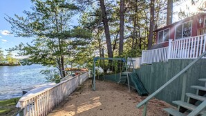 Une zone de plage sablonneuse avec une balançoire, un petit toboggan et une terrasse en bois dotée de rampes.