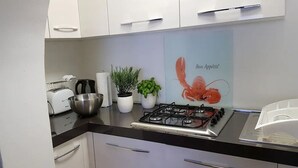 Et moderne køkken med hvide skabe, en gasblus, en brødrister og en potteplante.