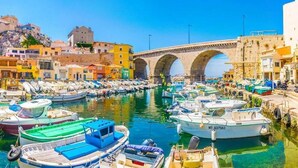 Un port où sont amarrés des bateaux, un pont de pierre et des bâtiments qui bordent la rive.