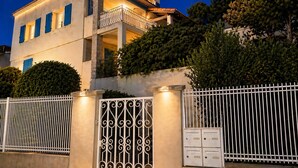 Un immeuble à plusieurs étages doté d’un balcon, d’une entrée sécurisée par un portail et d’une clôture blanche.