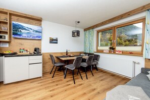 Cocina moderna con comedor, piso de madera y un amplio ventanal con vistas a árboles y montañas.