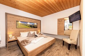 Un dormitorio con cabecera de madera, una cama grande, una silla, un televisor y una ventana con vistas a un paisaje montañoso.