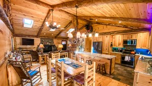 Interior rústico de una cabaña de madera con comedor, cocina y chimenea de piedra.