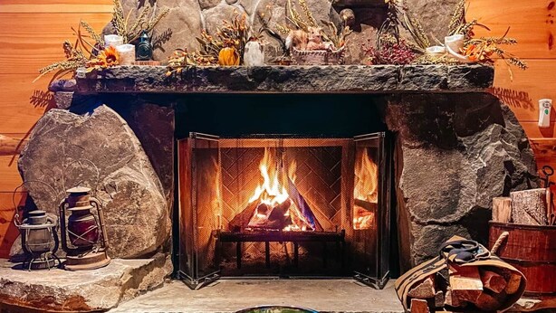 Una chimenea de piedra con fuego, una mesa con una pizza y un tazón de ensalada al frente.