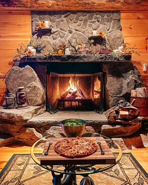 A stone fireplace with a fire, a table with a pizza, and a bowl of salad in front.