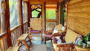 Interior de una cabaña de madera con un porche que tiene muebles de madera, una alfombra tejida y vistas al exterior.