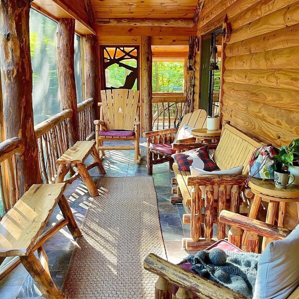 A wooden cabin interior with a porch area featuring wooden furniture, a woven rug, and a view of the outdoors.