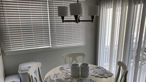 Ein Essbereich mit einem runden Tisch, Stühlen, einer Chandelüster und einem Fenster mit Jalousien.