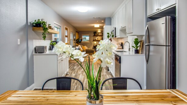 A modern kitchen with white cabinets, a stainless steel refrigerator, and a dining table with chairs.