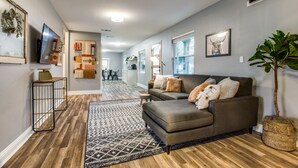 A modern living room with a grey sofa, patterned rug, and a large plant.