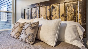 A bedroom with a wooden headboard, patterned bedding, and a view of the outside.