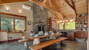 A rustic kitchen with a stone fireplace, wooden beams, and a large dining table set for four. - Mountain Bear Lodge At Northstar - TLUXP (Truckee)