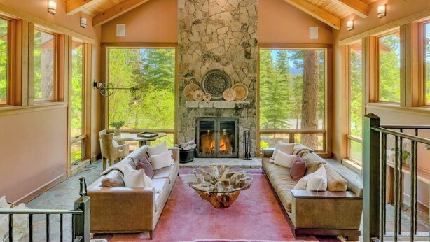 A cozy interior with a stone fireplace, wooden ceiling beams, and large windows offering a view of the outdoors. - Mountain Bear Lodge At Northstar - TLUXP (Truckee)