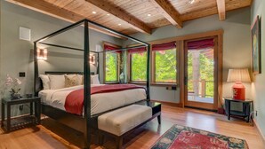 A four-poster bed with a red and white bedspread, a wooden floor, and a view of greenery through large windows. - Mountain Bear Lodge At Northstar - TLUXP (Truckee)