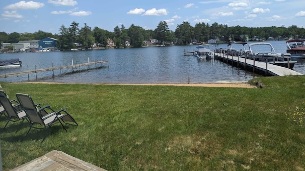 A lakeside view with a dock, boats, and a grassy area with chairs. - Winnisquam Lakeside Retreat w/Sandy Beach & Boat Docks (Tilton)