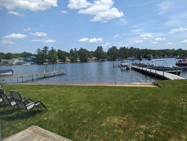A lakeside view with a dock, boats, and a grassy area with chairs.