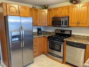 A kitchen with wooden cabinets, stainless steel appliances including a refrigerator, microwave, stove, oven, and dishwasher.