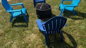 A lakeside dock with several boats, a grassy area with blue Adirondack chairs, and a round table. - Winnisquam Lakeside Retreat w/Sandy Beach & Boat Docks (Tilton)