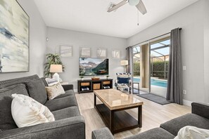 A modern living room with a sofa, coffee table, TV, and a view of a swimming pool.